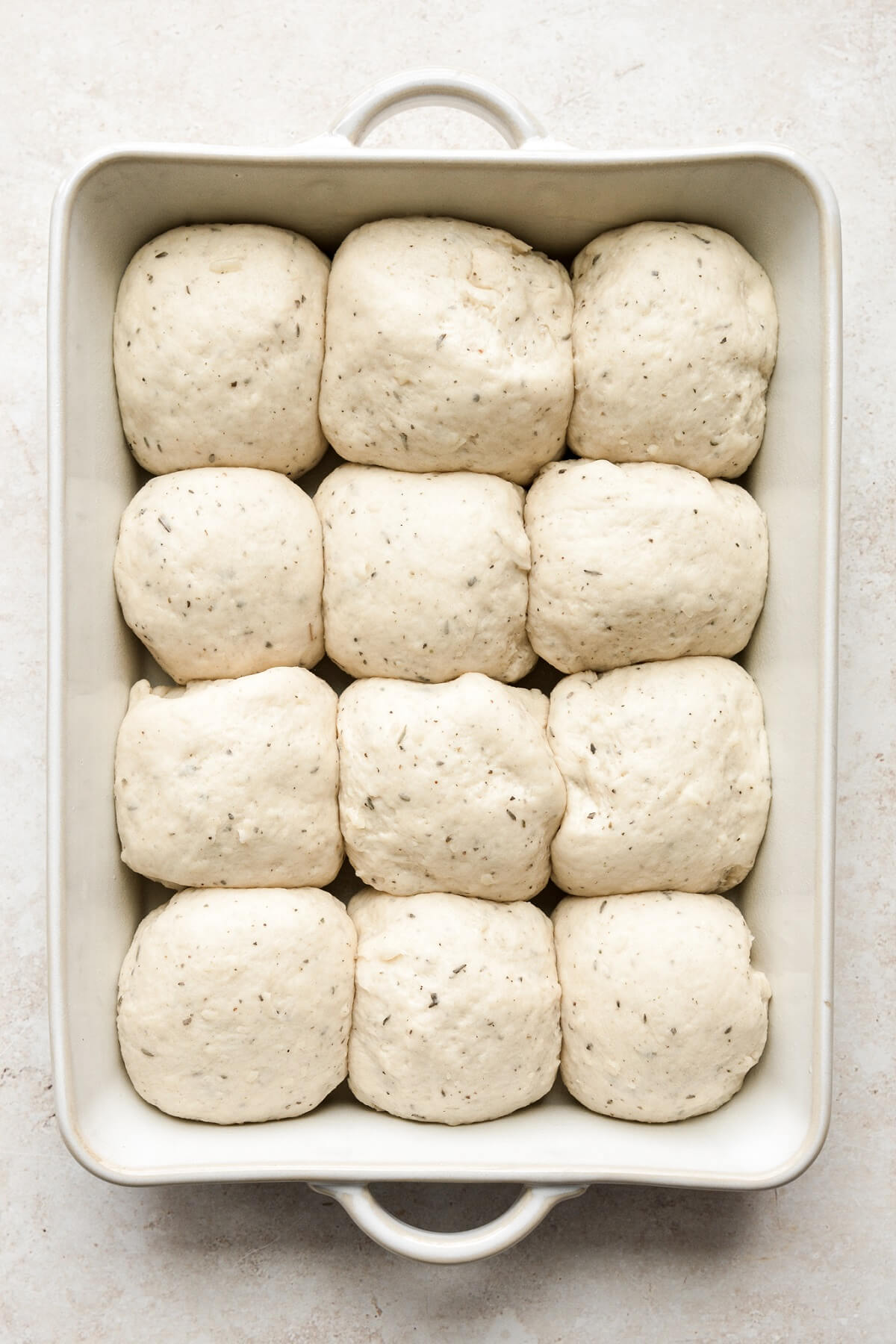 Garlic herb bread rolls rising in a baking pan.