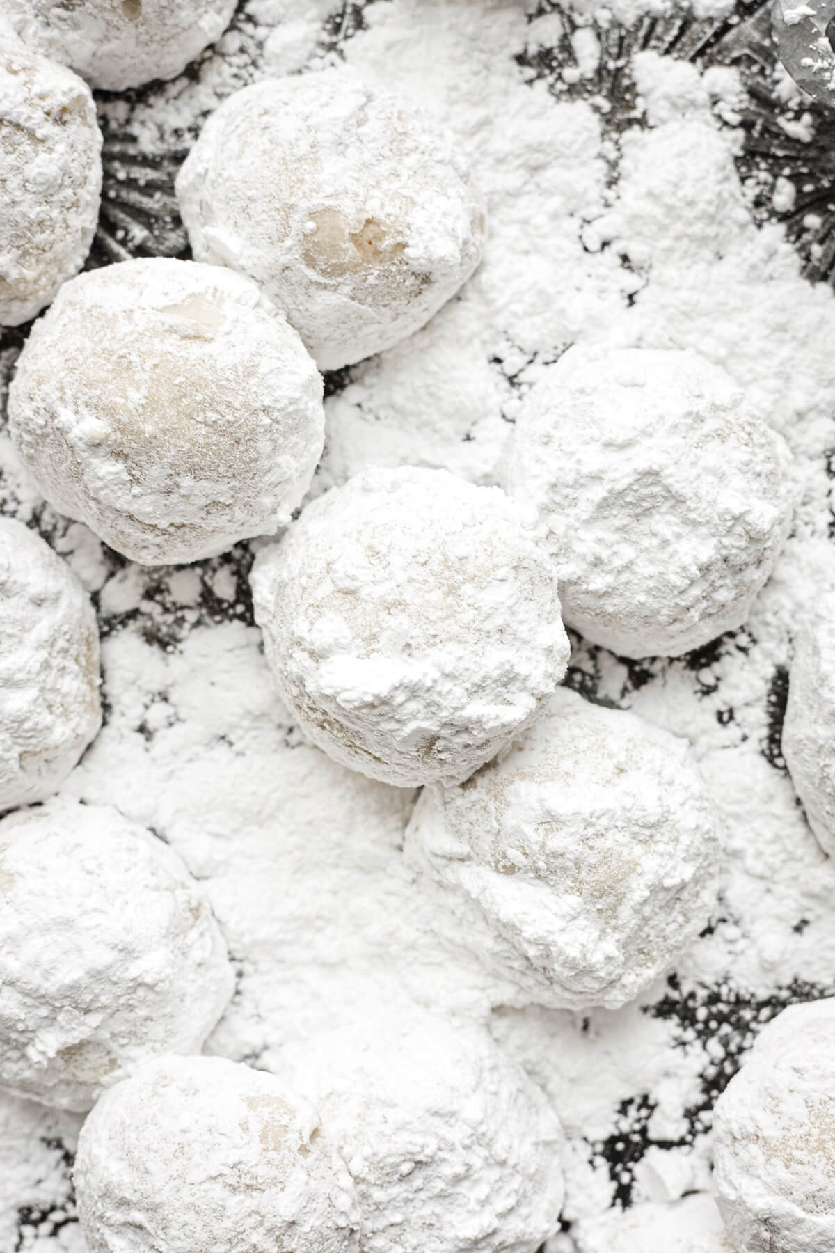 Snowball cookies on a tray of powdered sugar.
