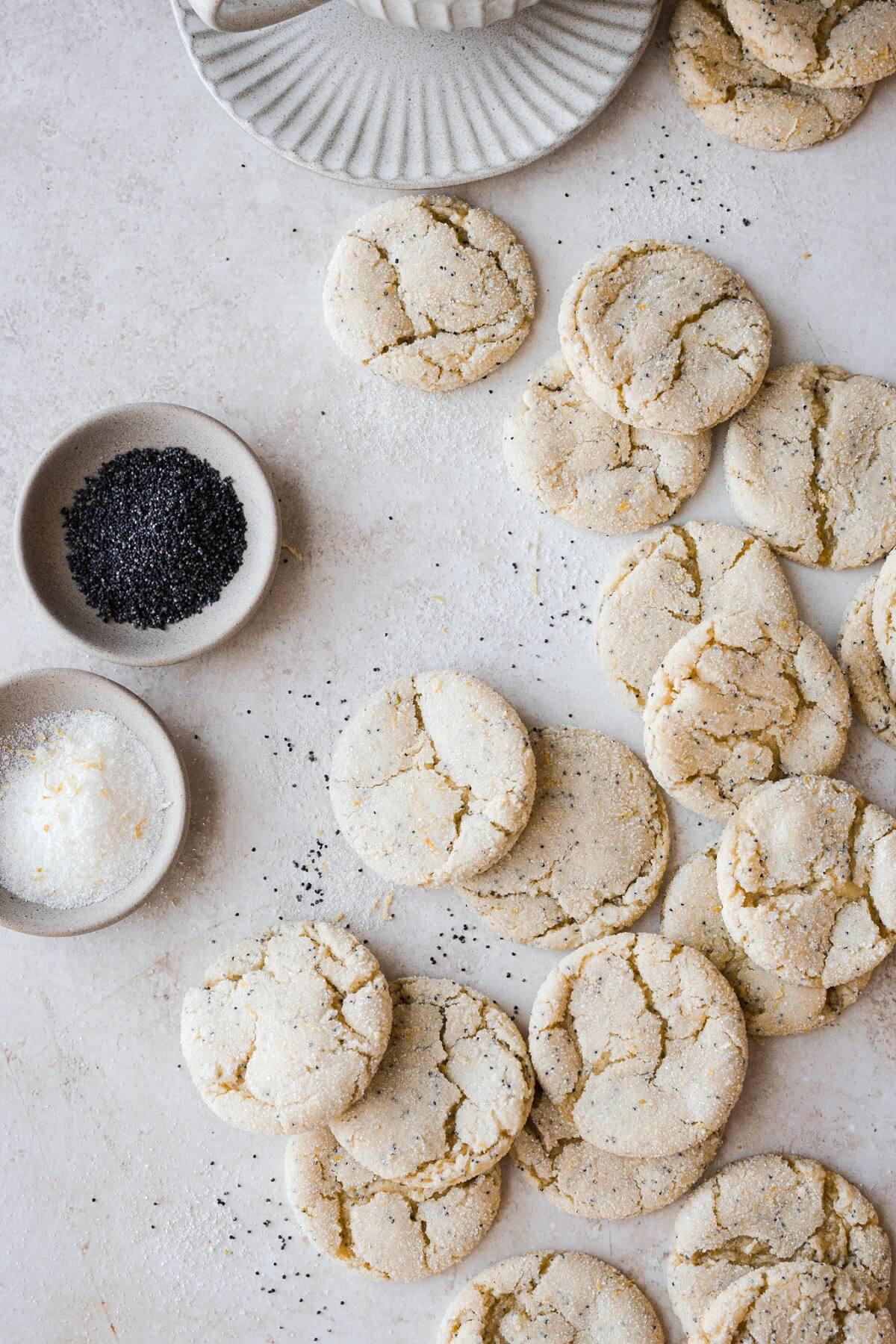 Lemon poppy seed cookies next to bowls of poppy seeds and lemon sugar.