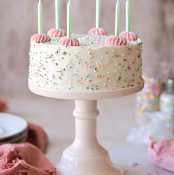 Mini sprinkle cake with green candles and pink piped buttercream.