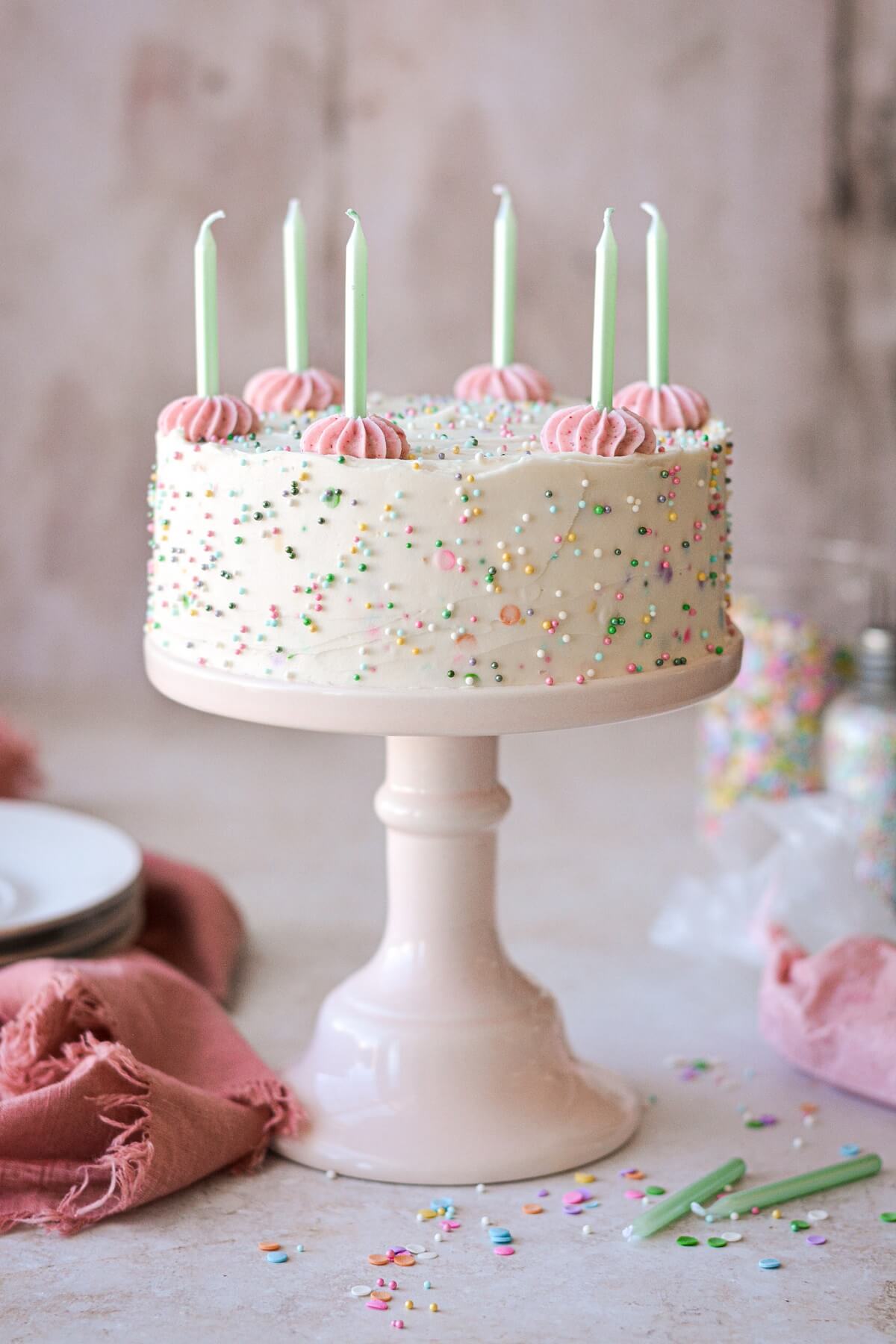 Mini sprinkle cake with green candles and pink piped buttercream.