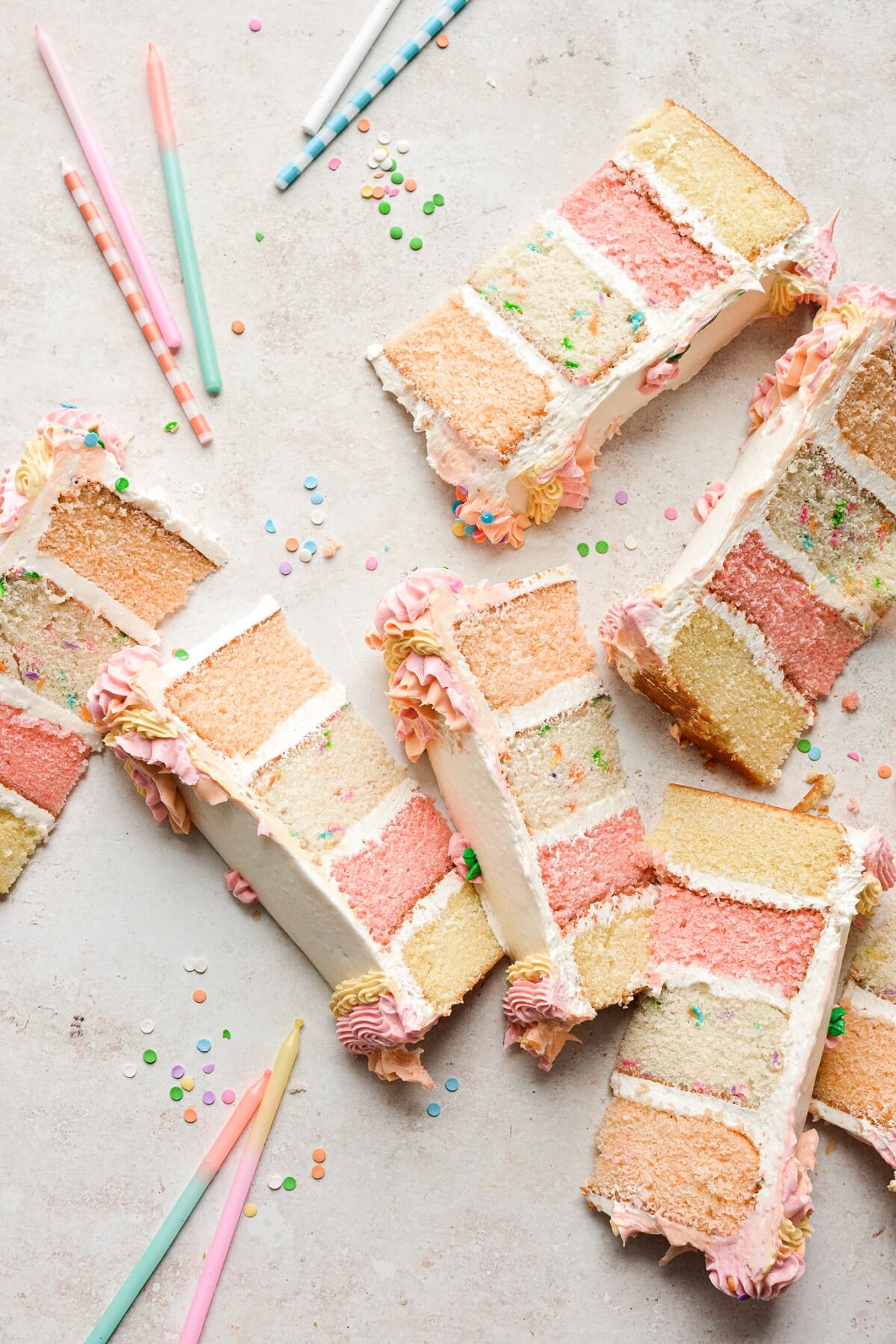 Slices of birthday cake surrounded by sprinkles and candles.