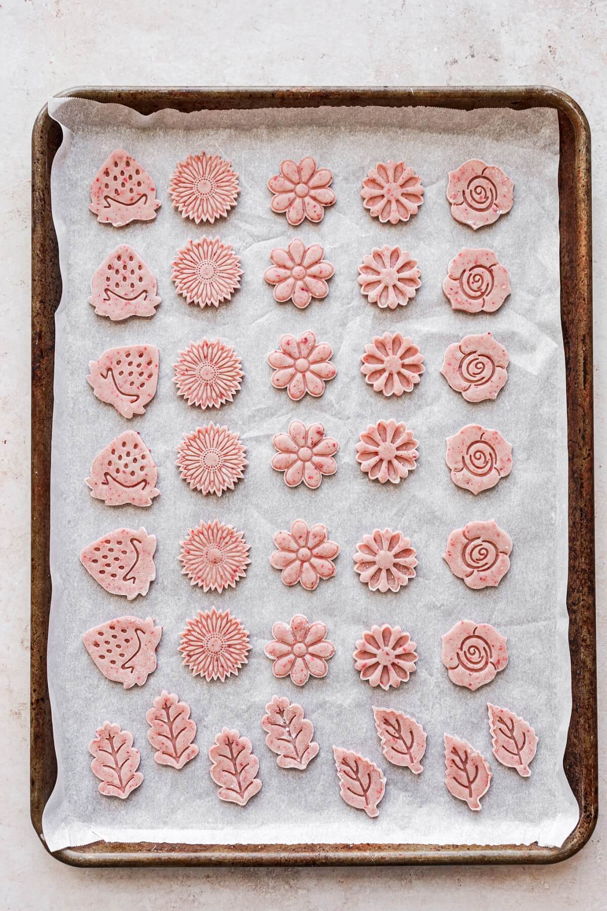 Flower shaped strawberry cutout cookies on a baking sheet.