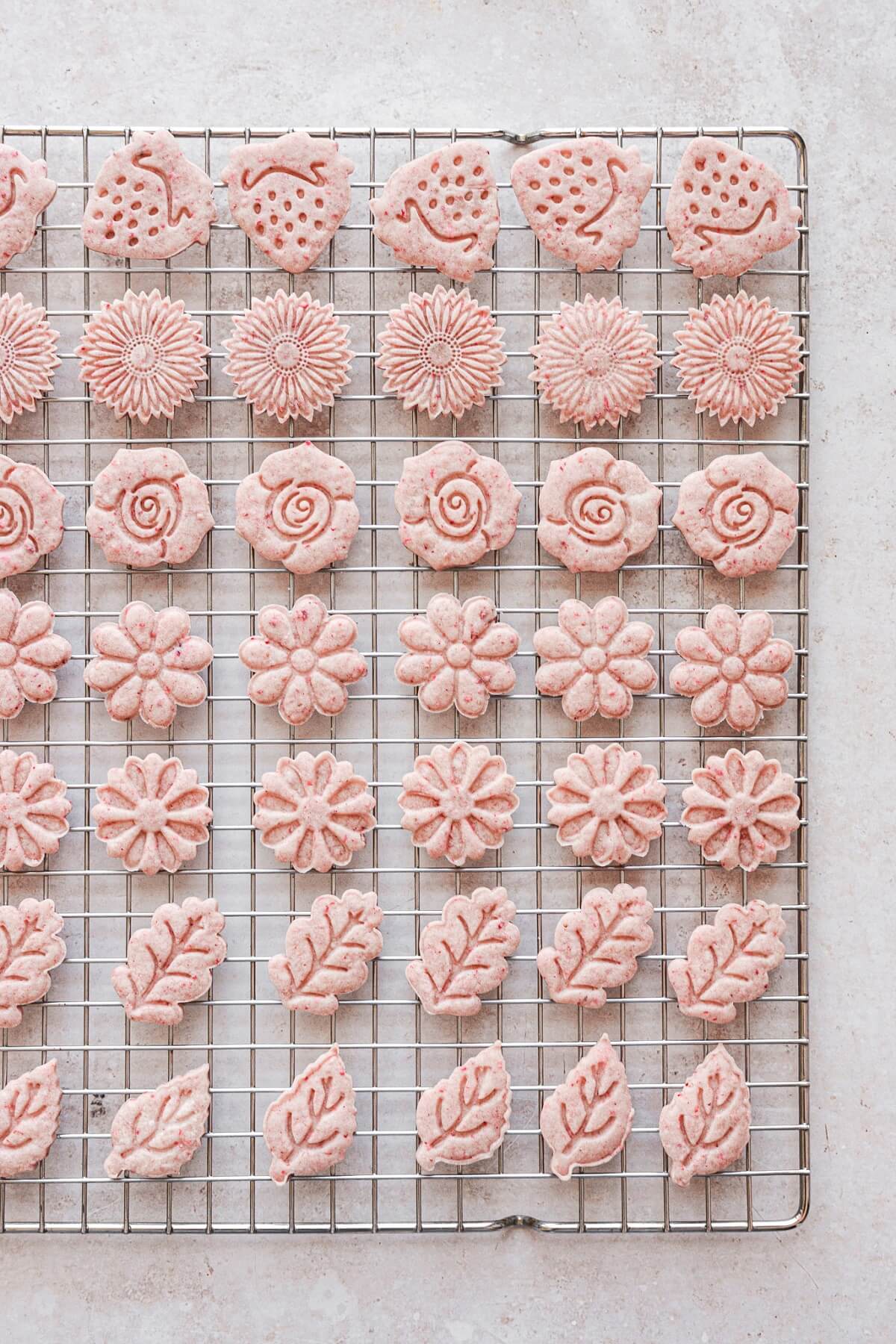 Flower shaped strawberry cutout cookies on a cooling rack.