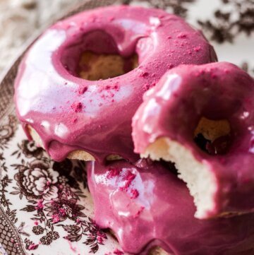 Vanilla cake donuts with blueberry icing, one with a bite taken.