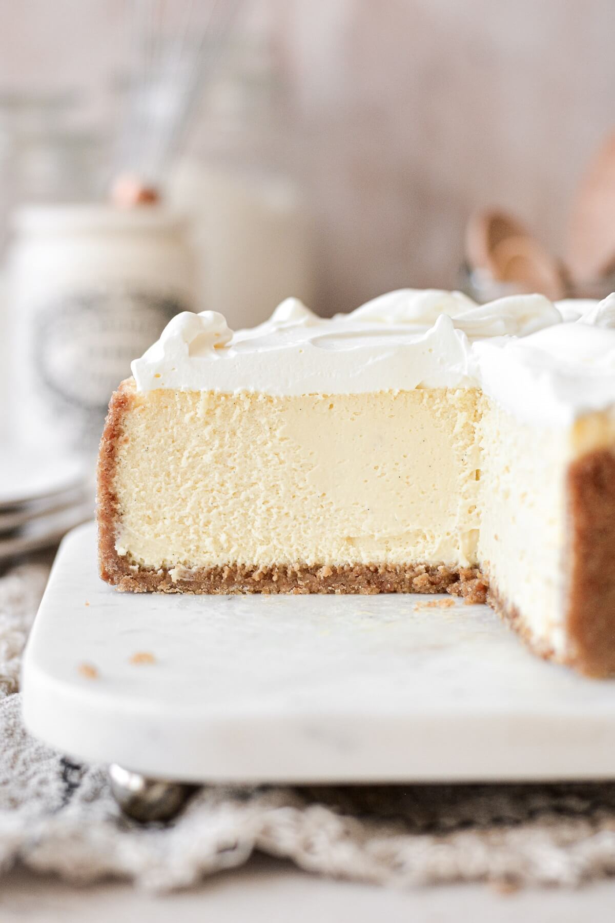 Creamy vanilla cheesecake topped with whipped cream, with a piece cut.