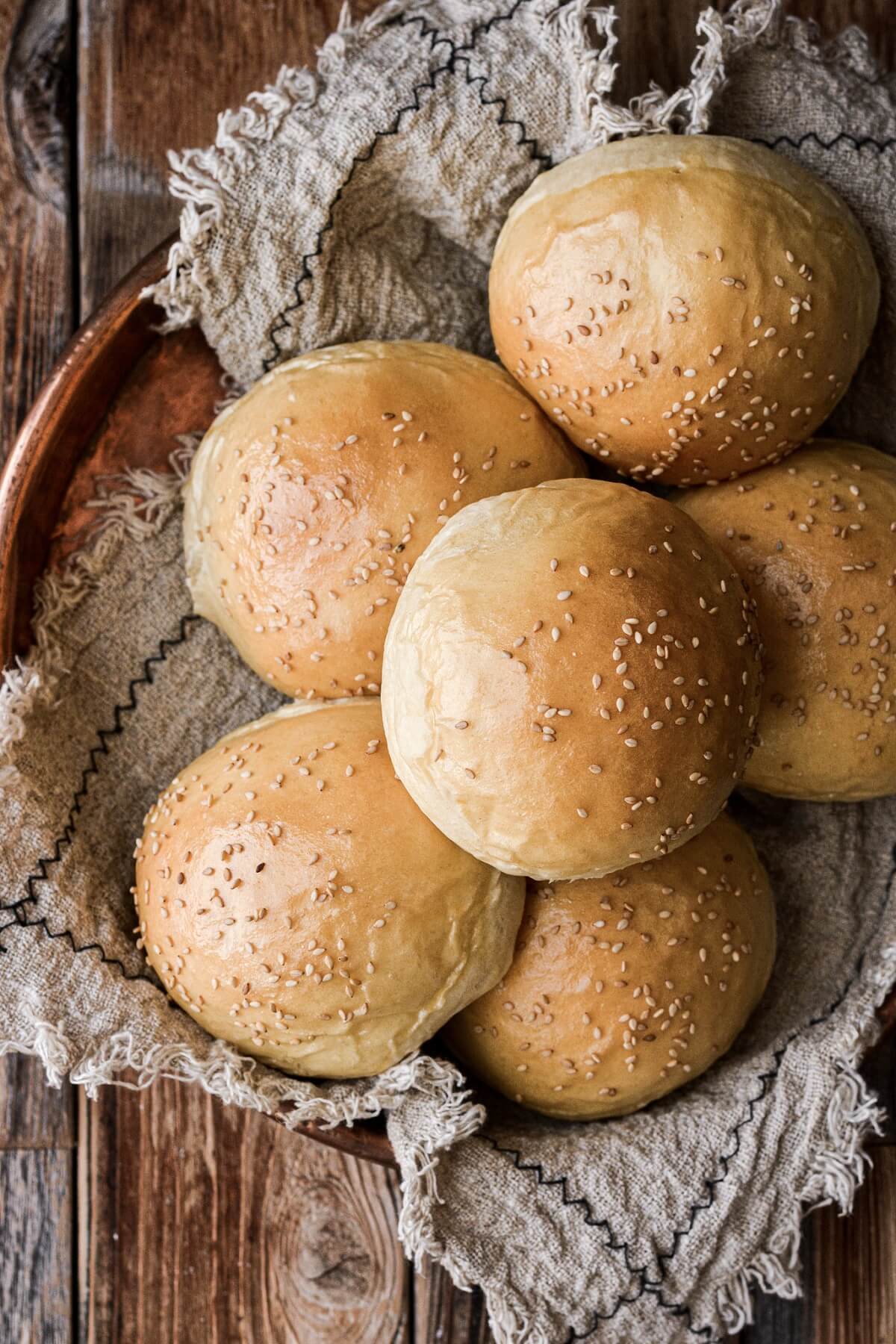 Brioche burger buns arranged in a copper tray with a linen.