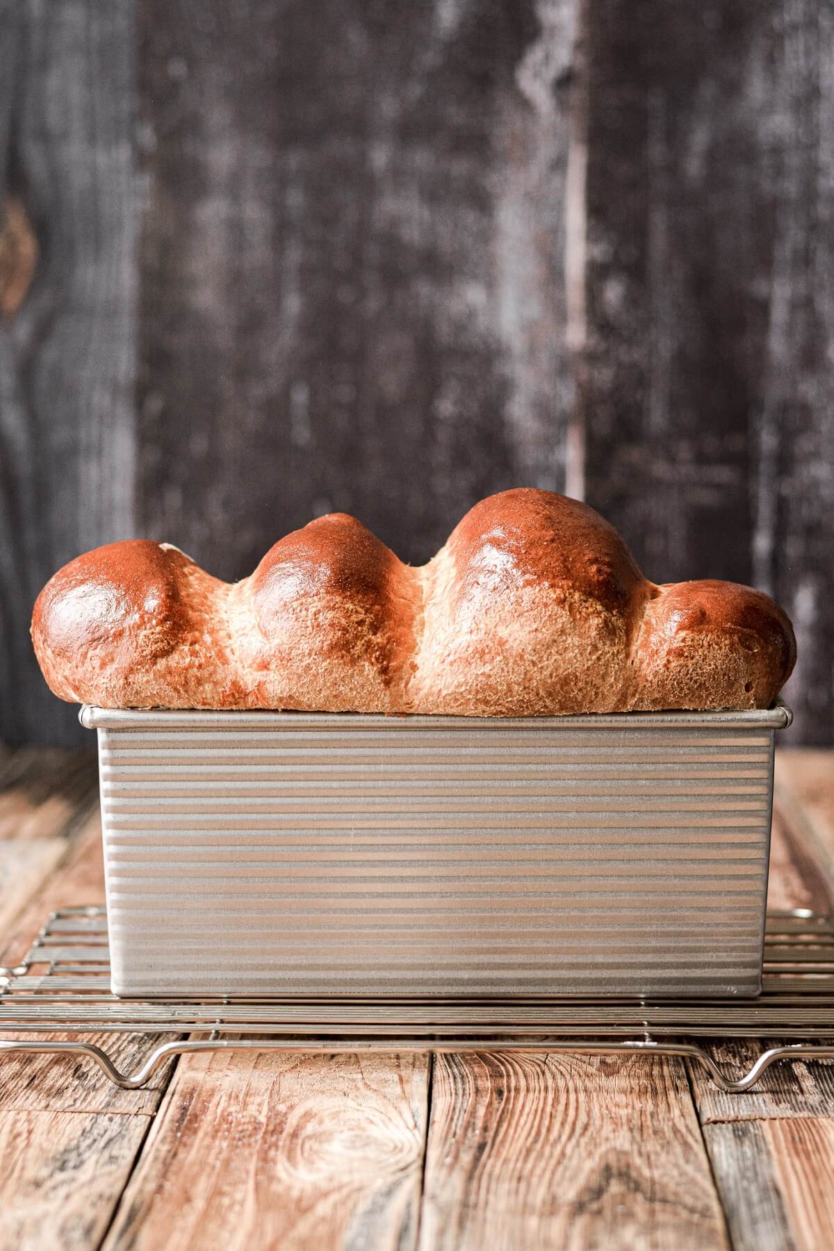 A baked loaf of milk bread puffing above a loaf pan.