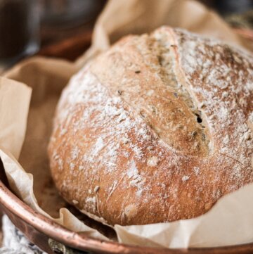 A rustic loaf of no knead caraway bread in a copper pan.