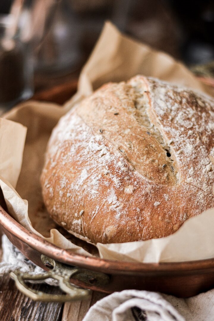 A rustic loaf of no knead caraway bread in a copper pan.