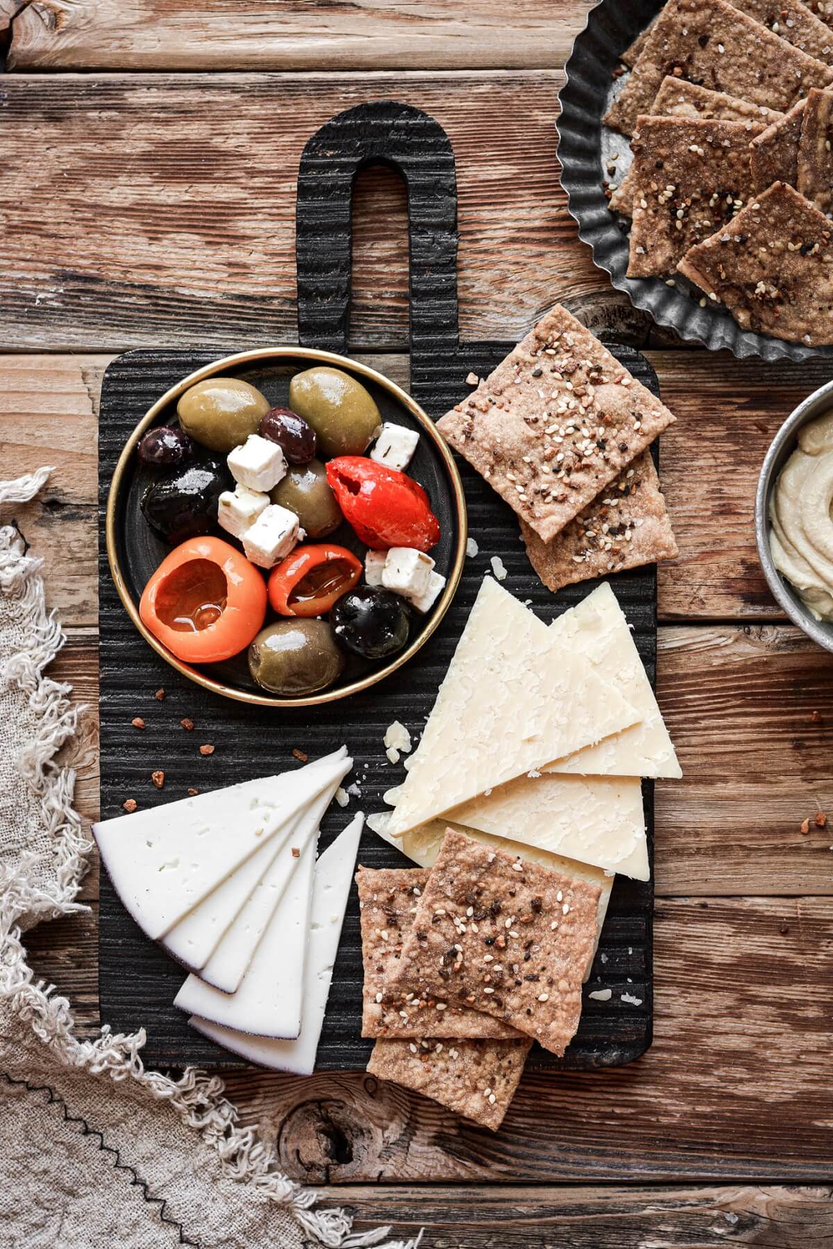 A cutting board with olives, cheese and homemade crackers.