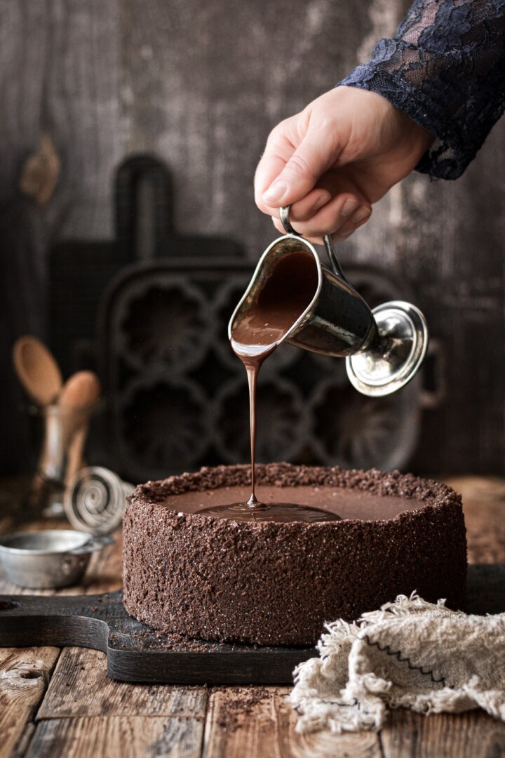 Chocolate ganache pouring on top of a chocolate cheesecake.
