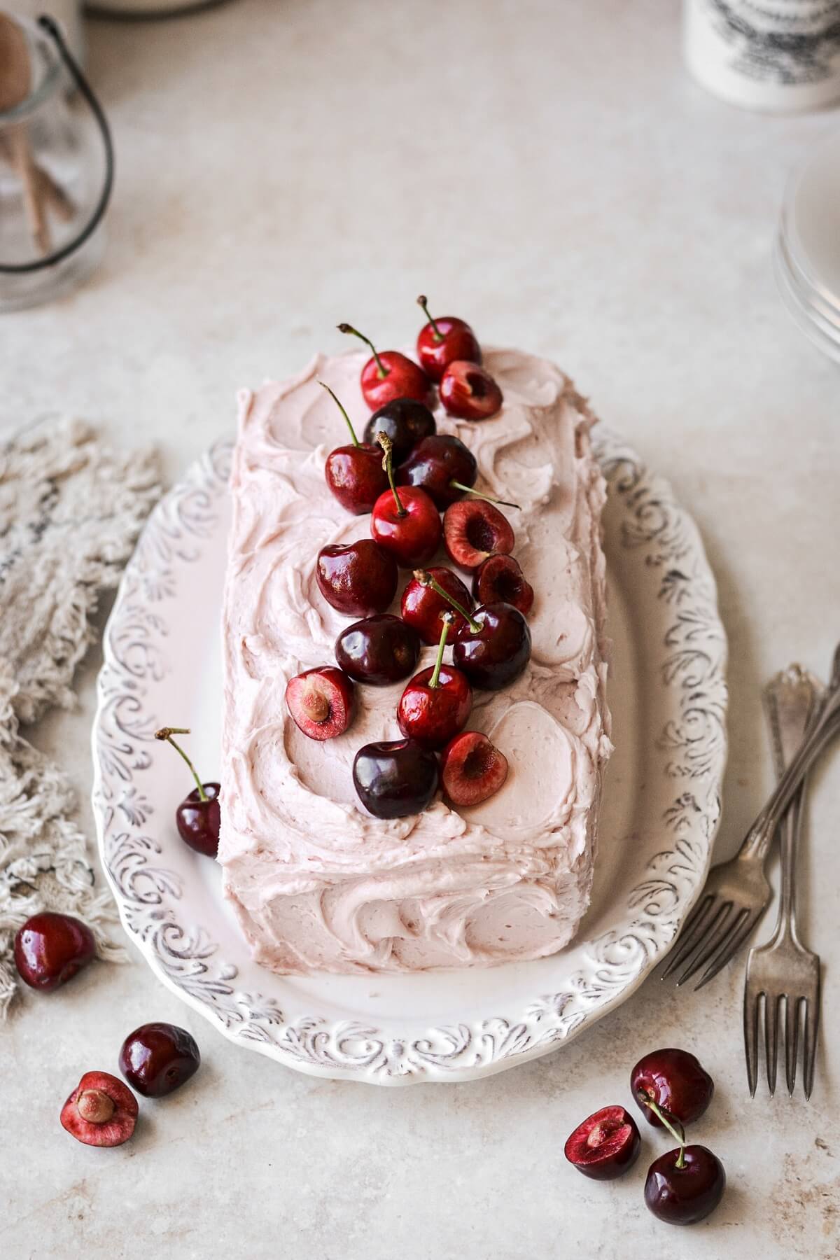 Cherries arranged on top of a pink frosted loaf cake.