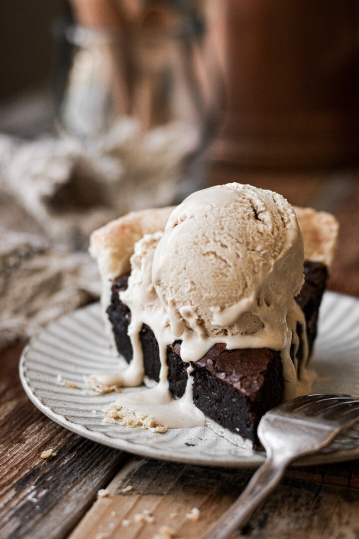 Ice cream melting on top of a slice of brownie pie.