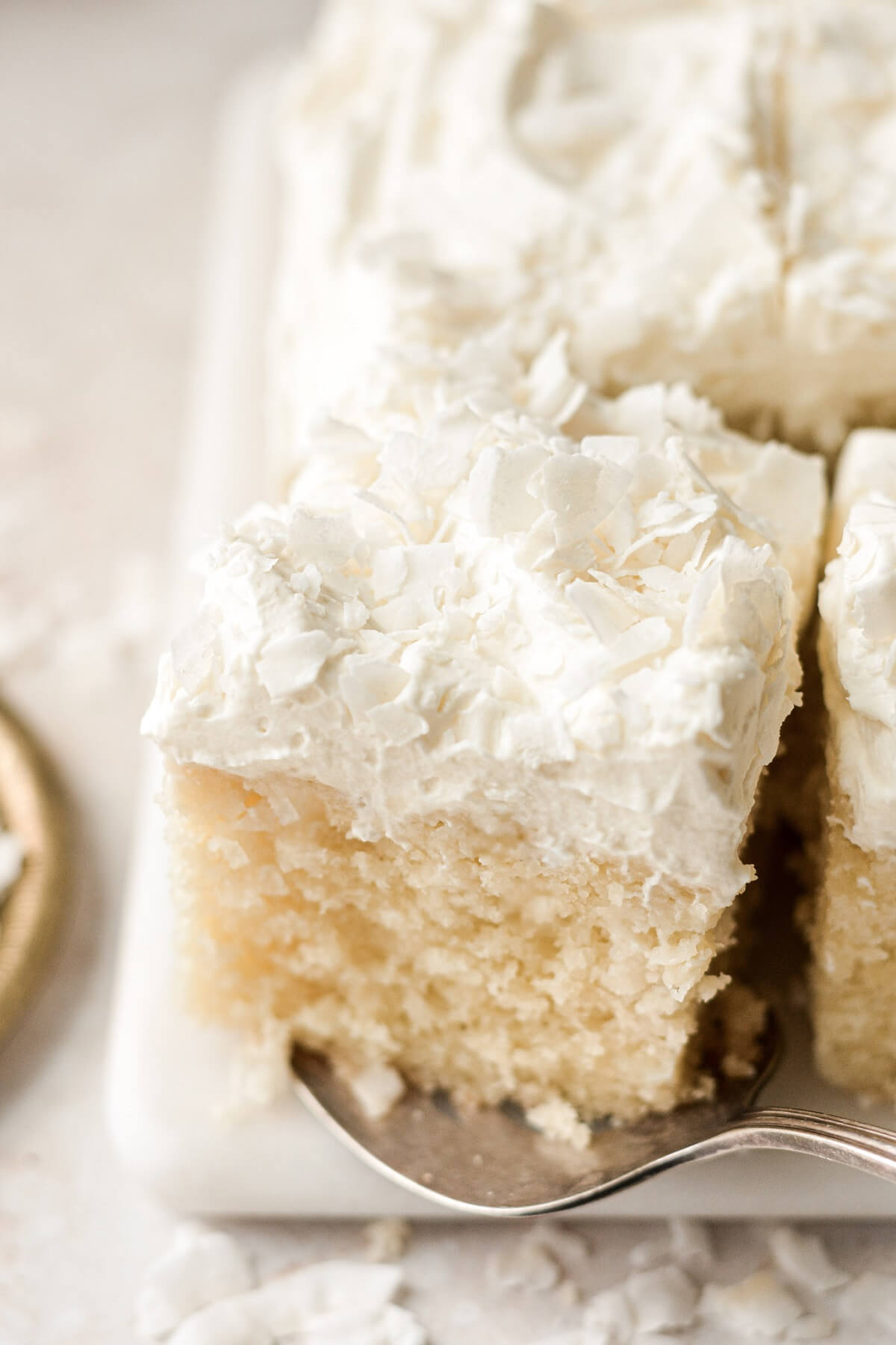 Squares of coconut cream sheet cake with mascarpone whipped cream and flaked coconut.