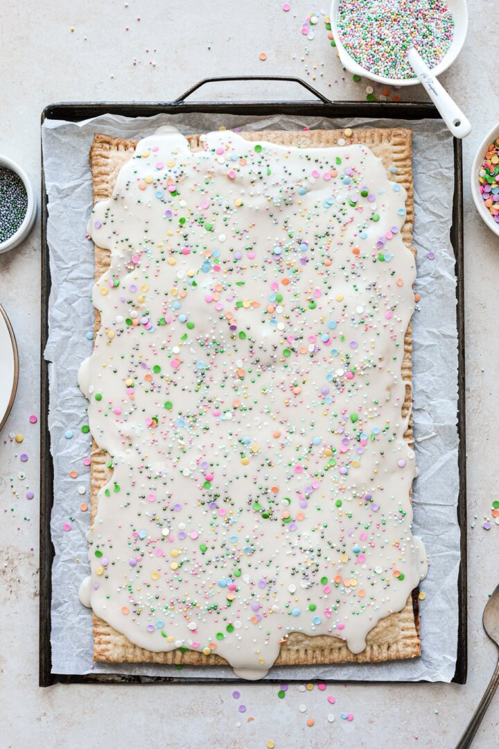 A big blueberry pop tart on a baking sheet with vanilla icing and sprinkles.