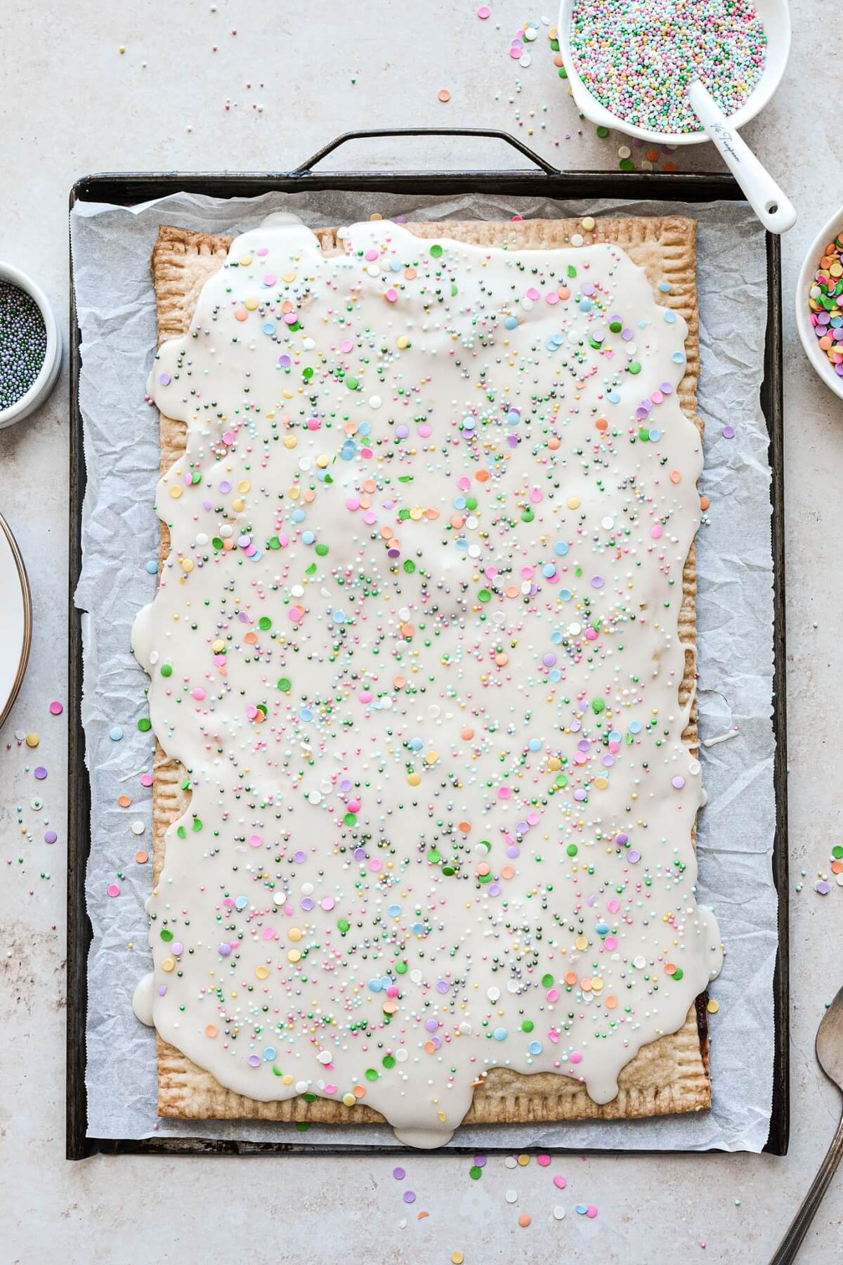 A big blueberry pop tart on a baking sheet with vanilla icing and sprinkles.