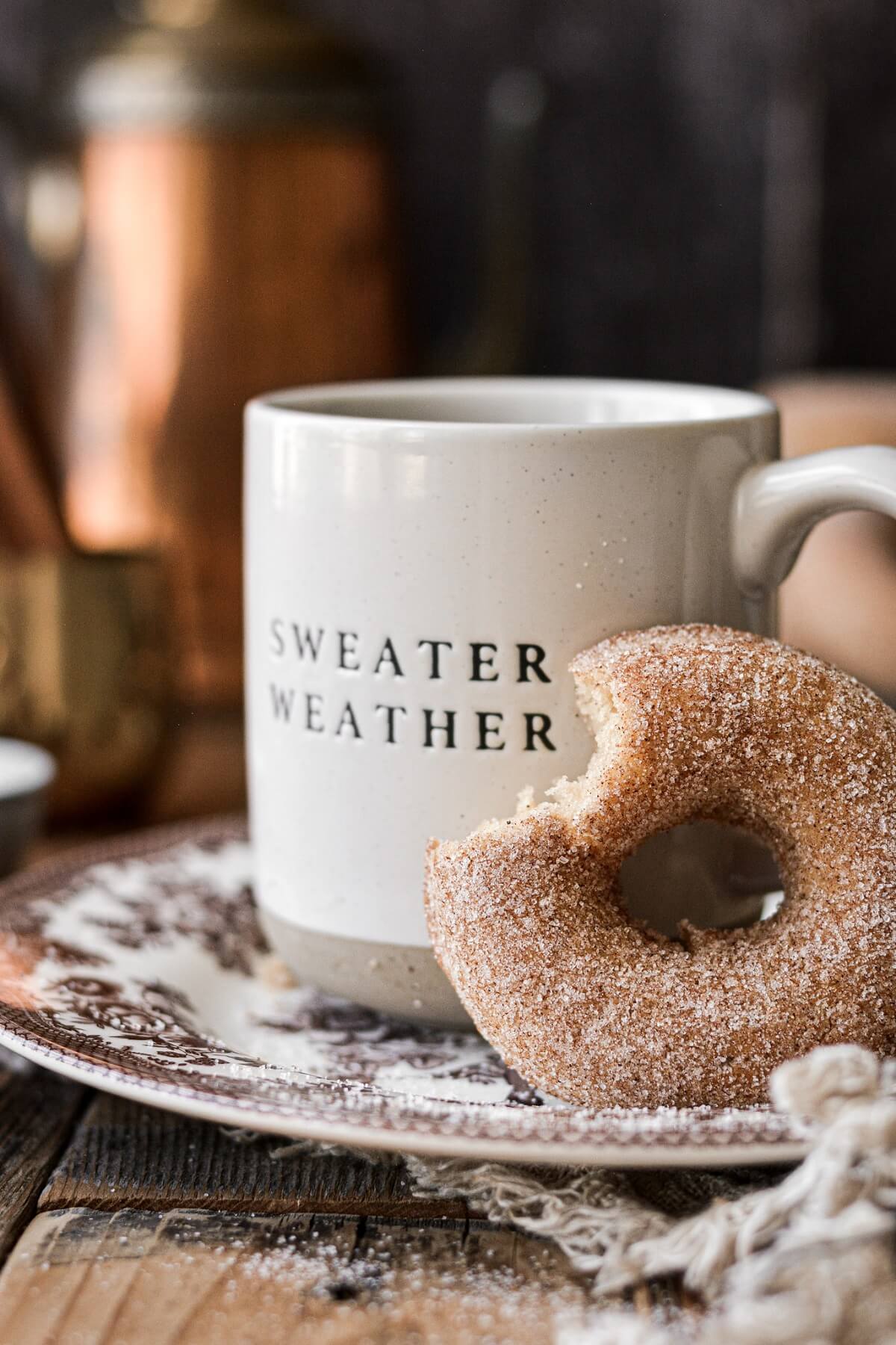 A cinnamon sugar donut next to a coffee cup that says "sweater weather".