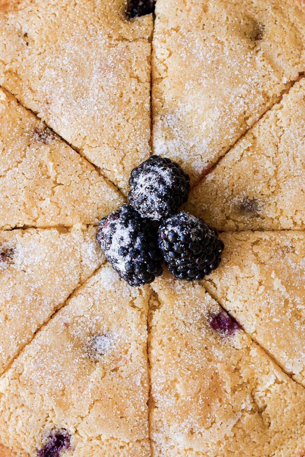 Blackberries on top of a blackberry cornbread cake cut into wedges.