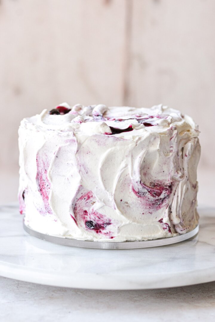 A cake frosted with whipped cream frosting swirled with blueberry jam.