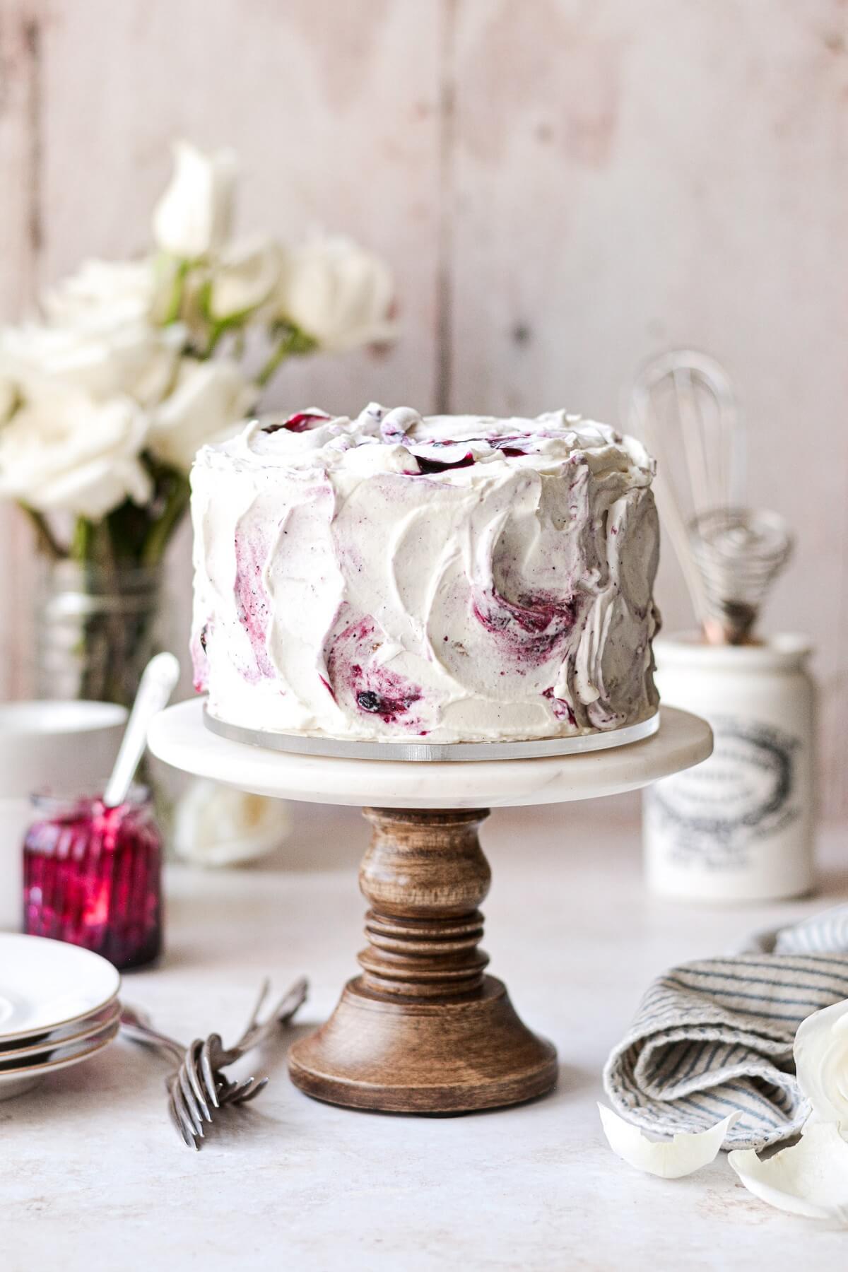 Blueberry jam and cream chantilly cake on a marble and wood cake stand.