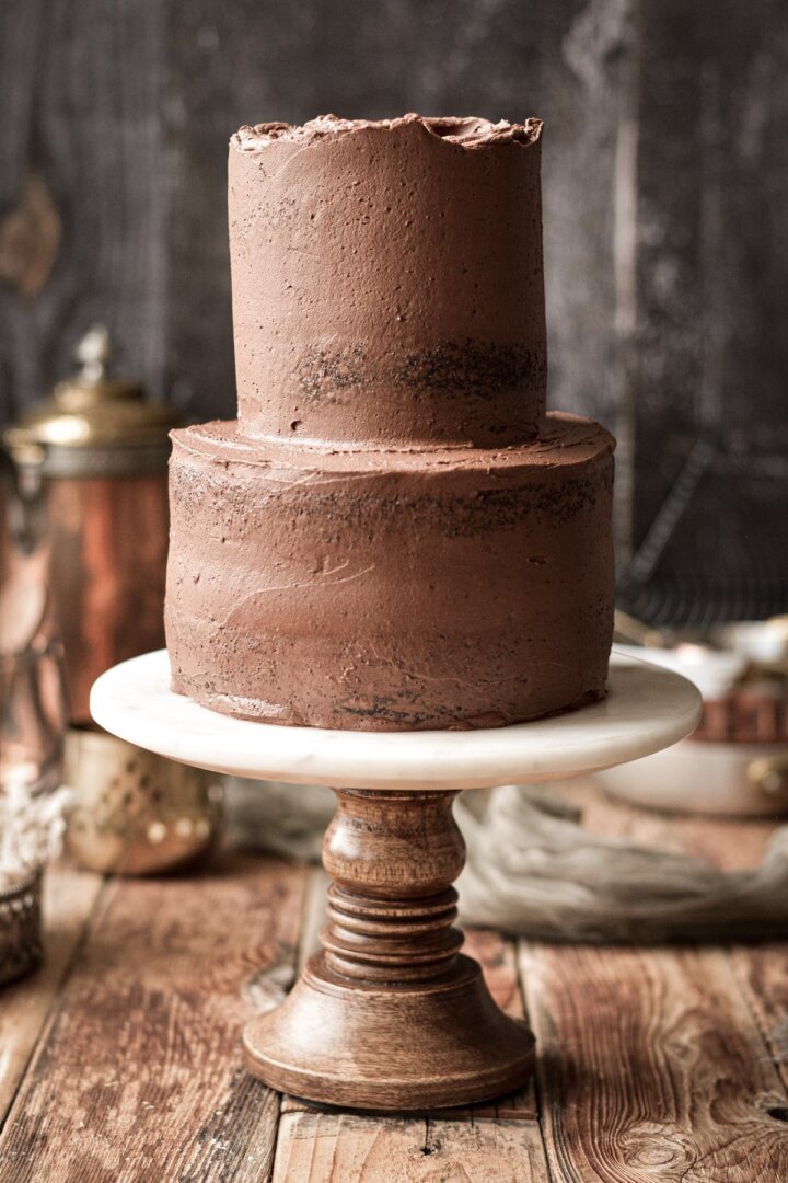 Crumb coat of chocolate buttercream on a two tiered chocolate cake.