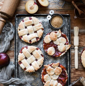 Mini plum pies with lattice crust, on a baking sheet.