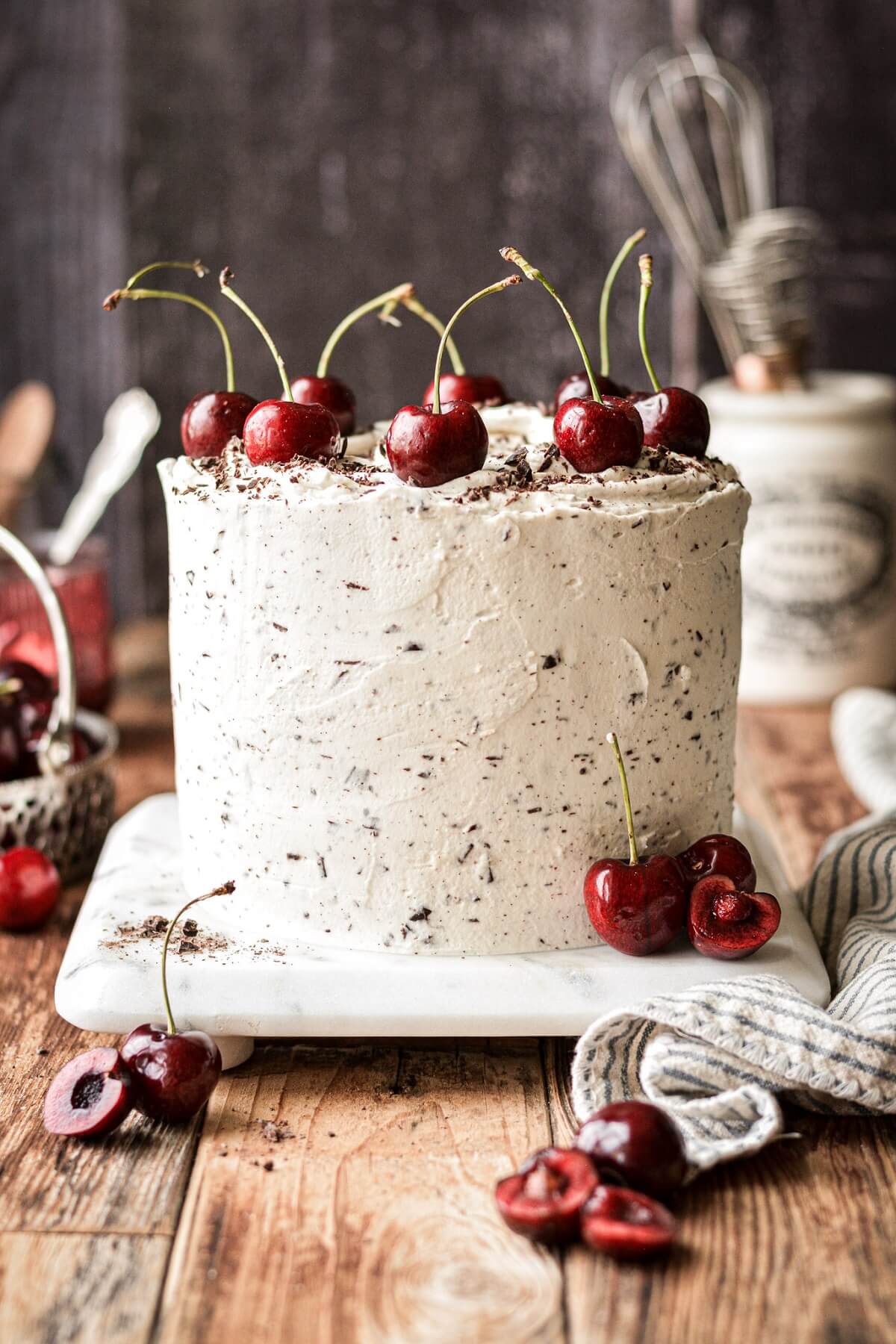White forest cake with chocolate chip whipped cream frosting and cherries on top.