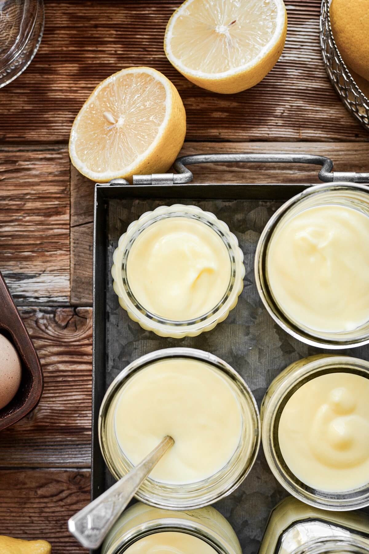 Glass jars of lemon pudding in a metal tray.