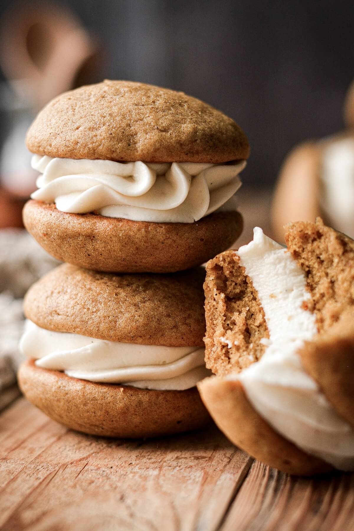 Pumpkin whoopie pies with cream cheese filling, one with a bite taken.