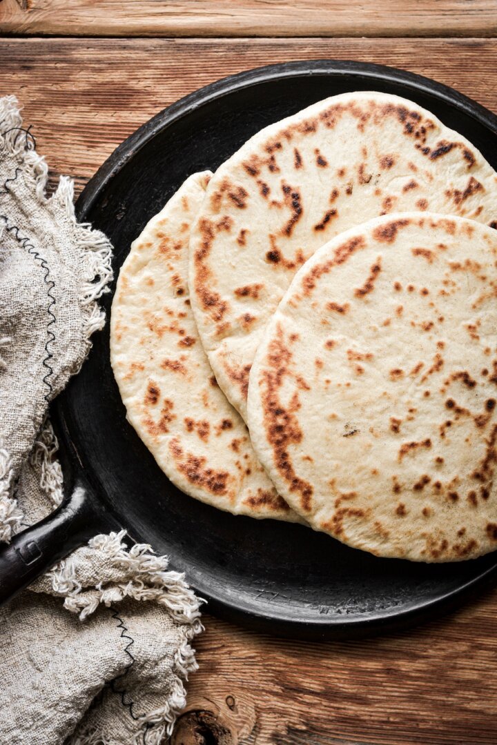 Homemade naan on a black skillet.