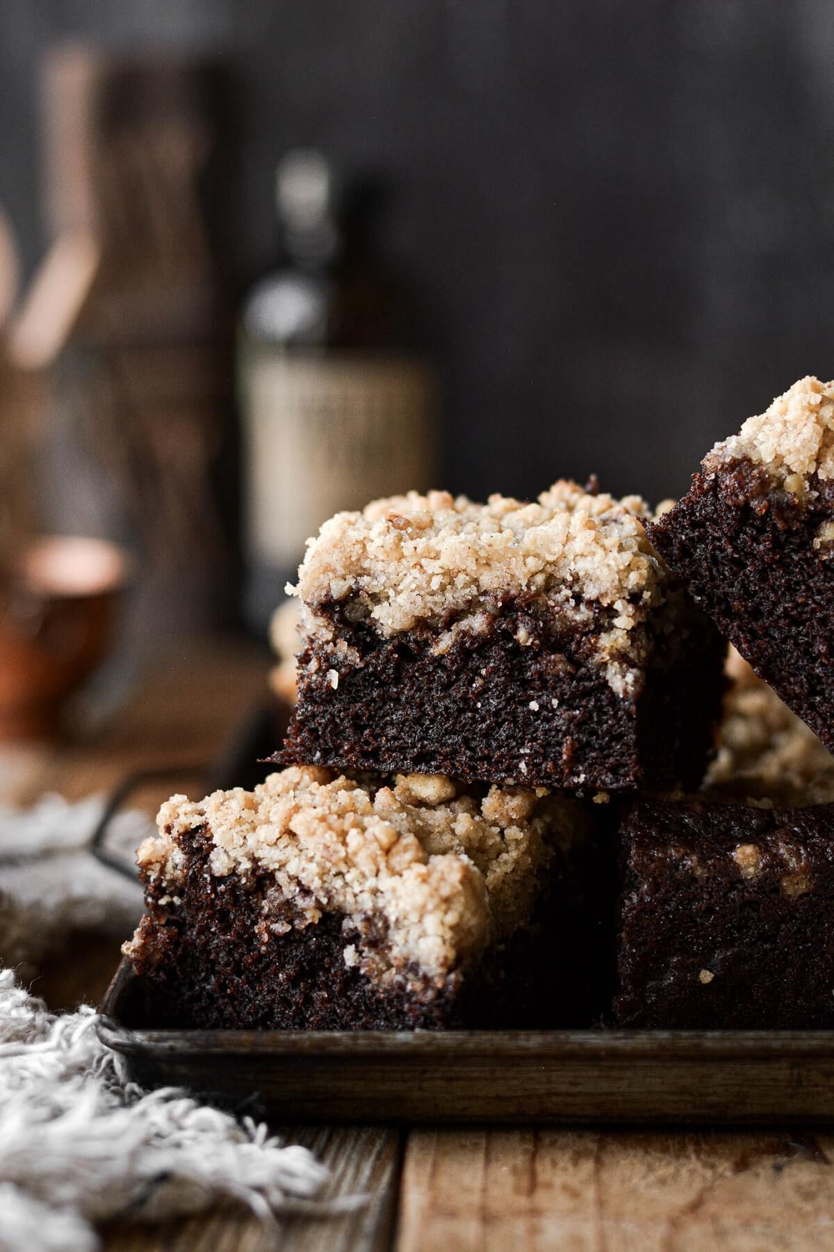 Squares of chocolate crumb cake with walnut streusel stacked on a baking sheet.