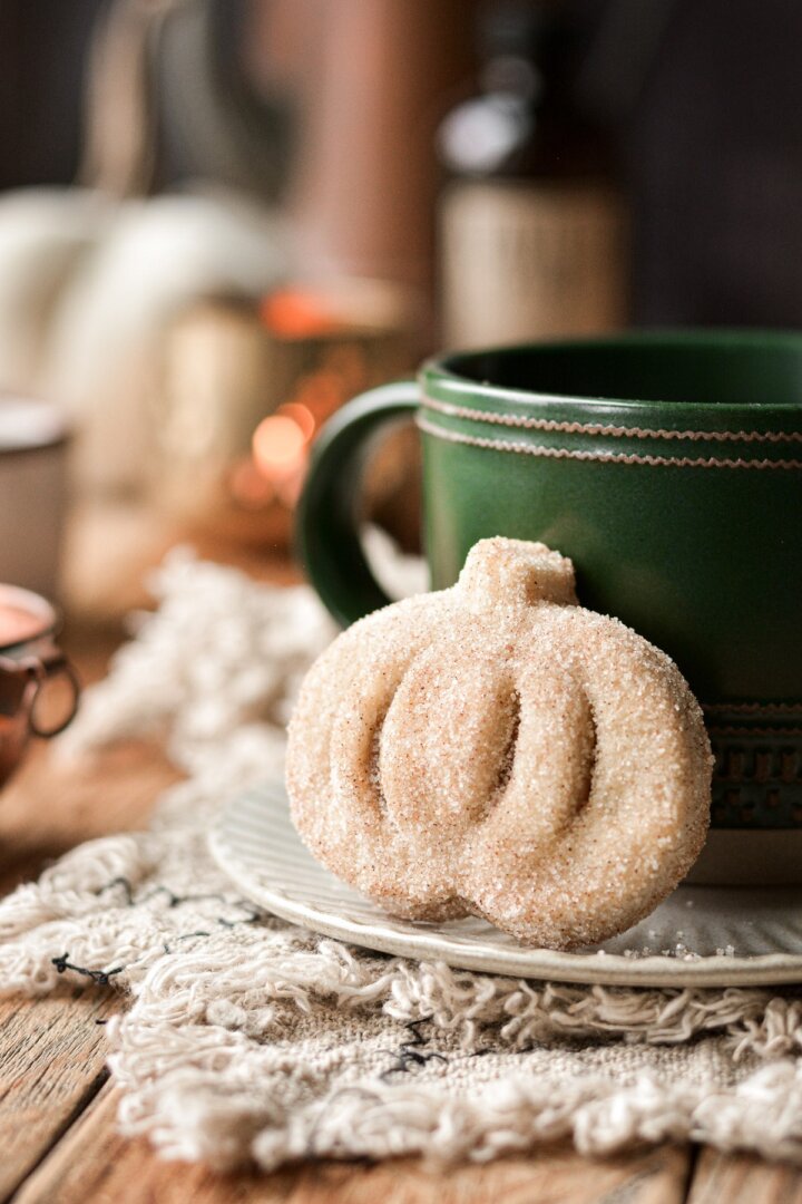Cinnamon sugar coated mini pumpkin pie leaning against a coffee cup.