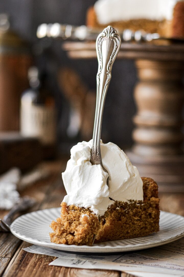 A piece of pumpkin cake with whipped cream, and a fork standing in the cake.