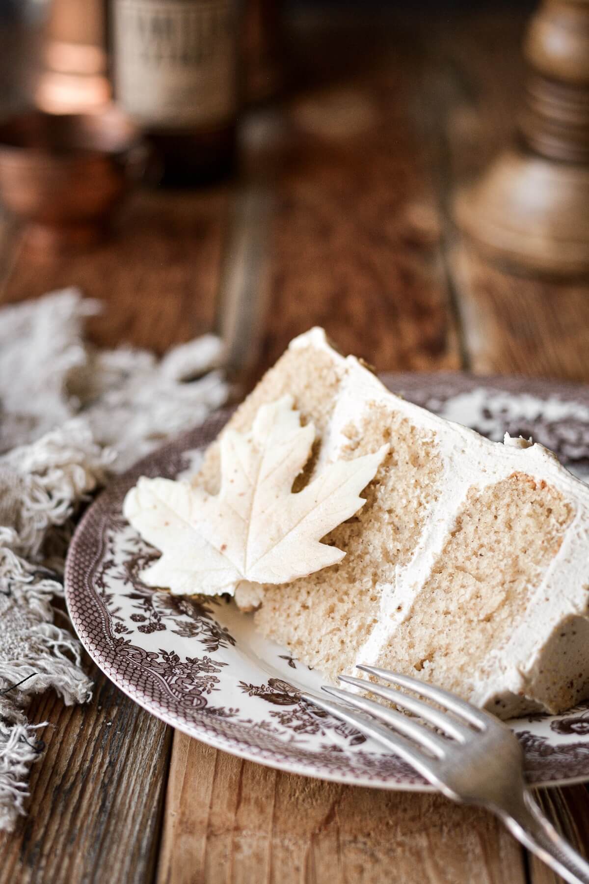A slice of white chocolate maple spice cake on a plate with a white chocolate leaf.