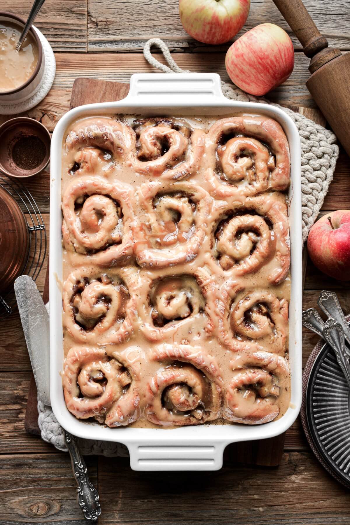 Apple pie cinnamon rolls with caramel icing in a baking dish.