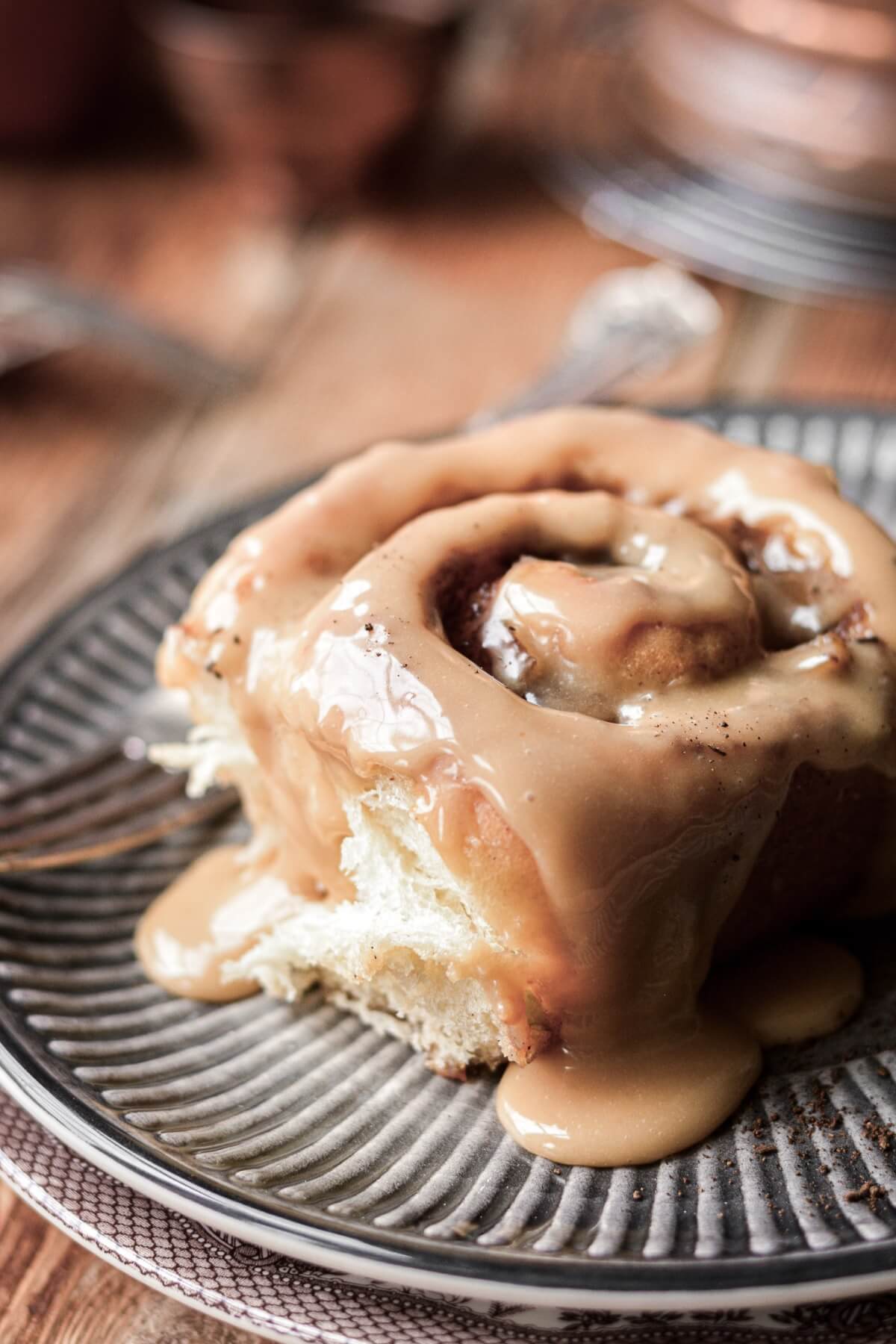 Apple pie cinnamon roll with caramel icing dripping onto a plate.