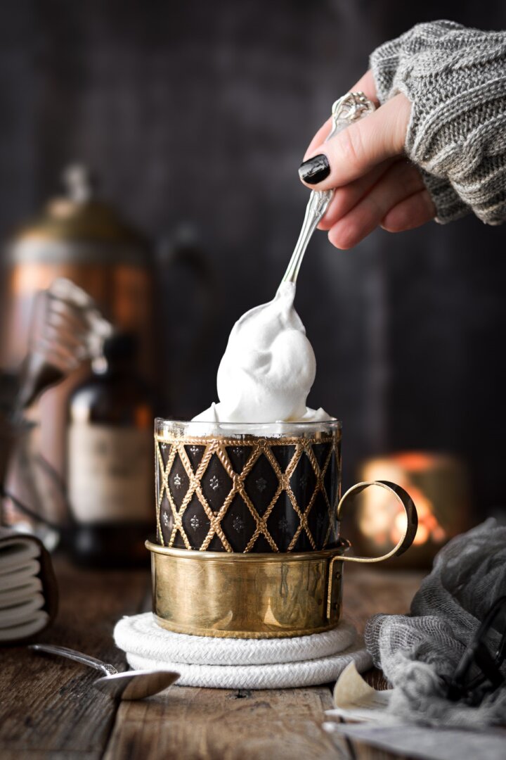 Whipped cream being spooned onto hot chocolate.