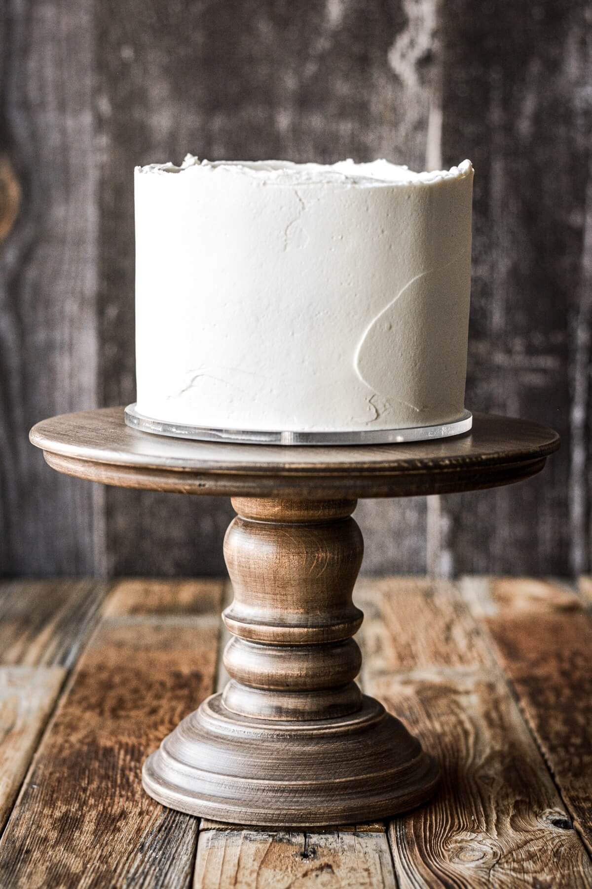 Vanilla buttercream frosted cake on a wooden cake stand.
