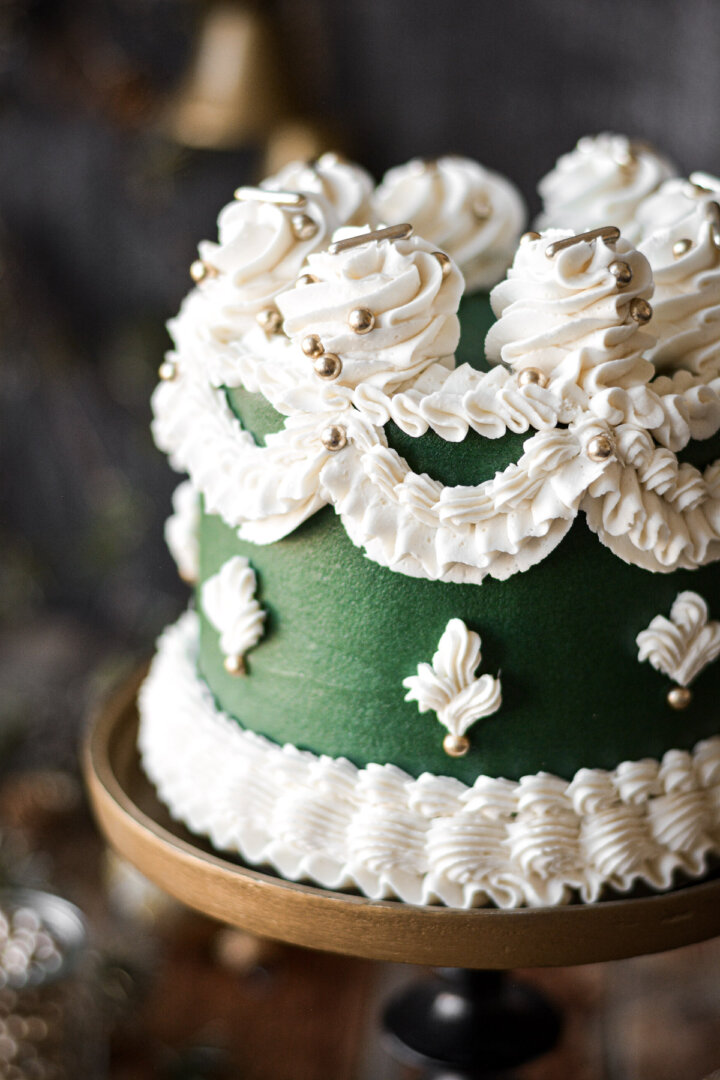 Fancy white buttercream piping and gold dragees on a green frosted cake.