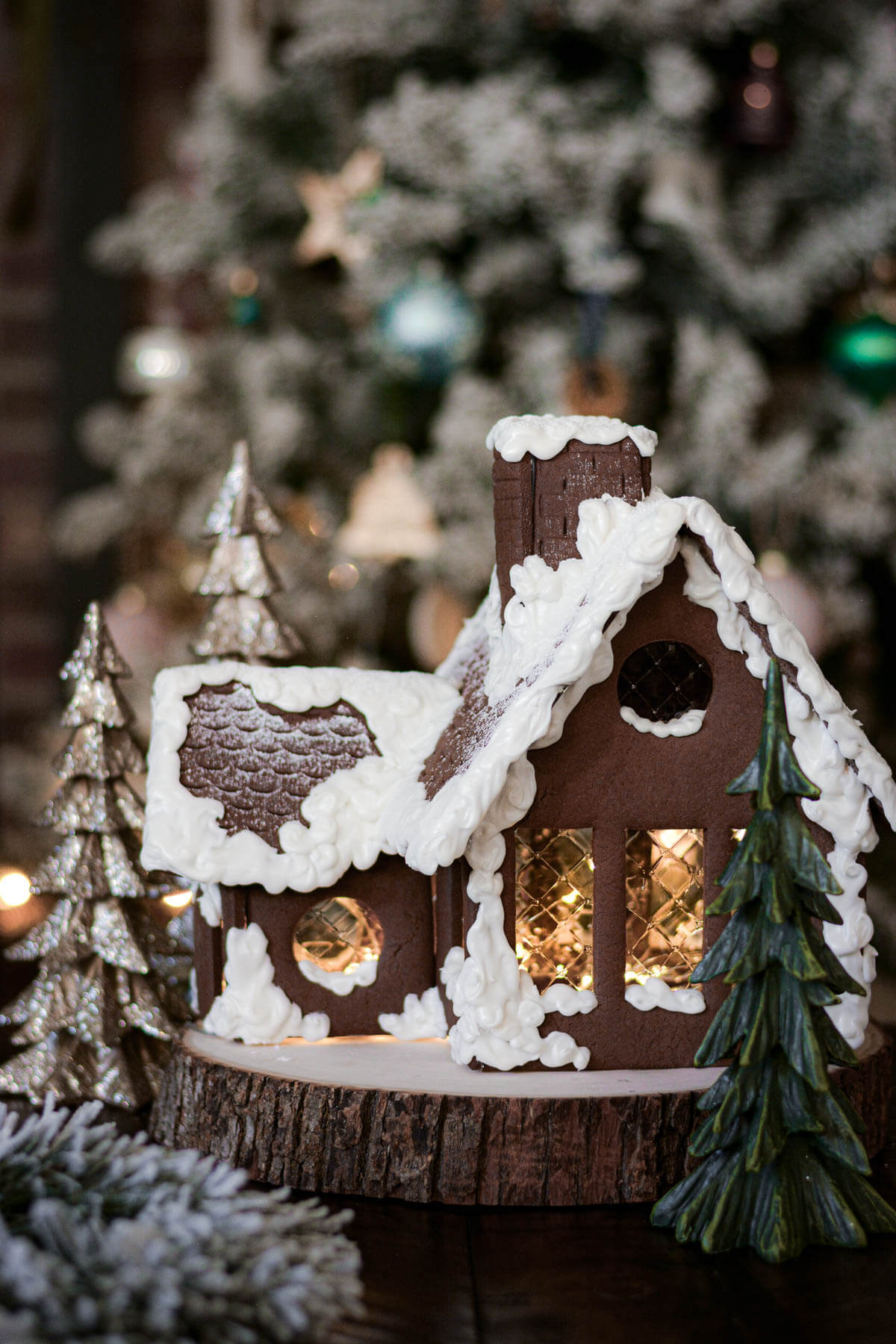 A homemade gingerbread house sitting in front of a Christmas tree.