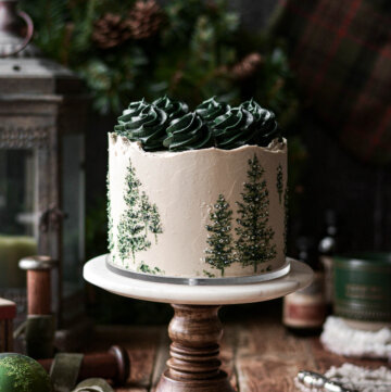 Chocolate maple cake with green evergreen trees painted onto the cake and green frosting swirls on top.