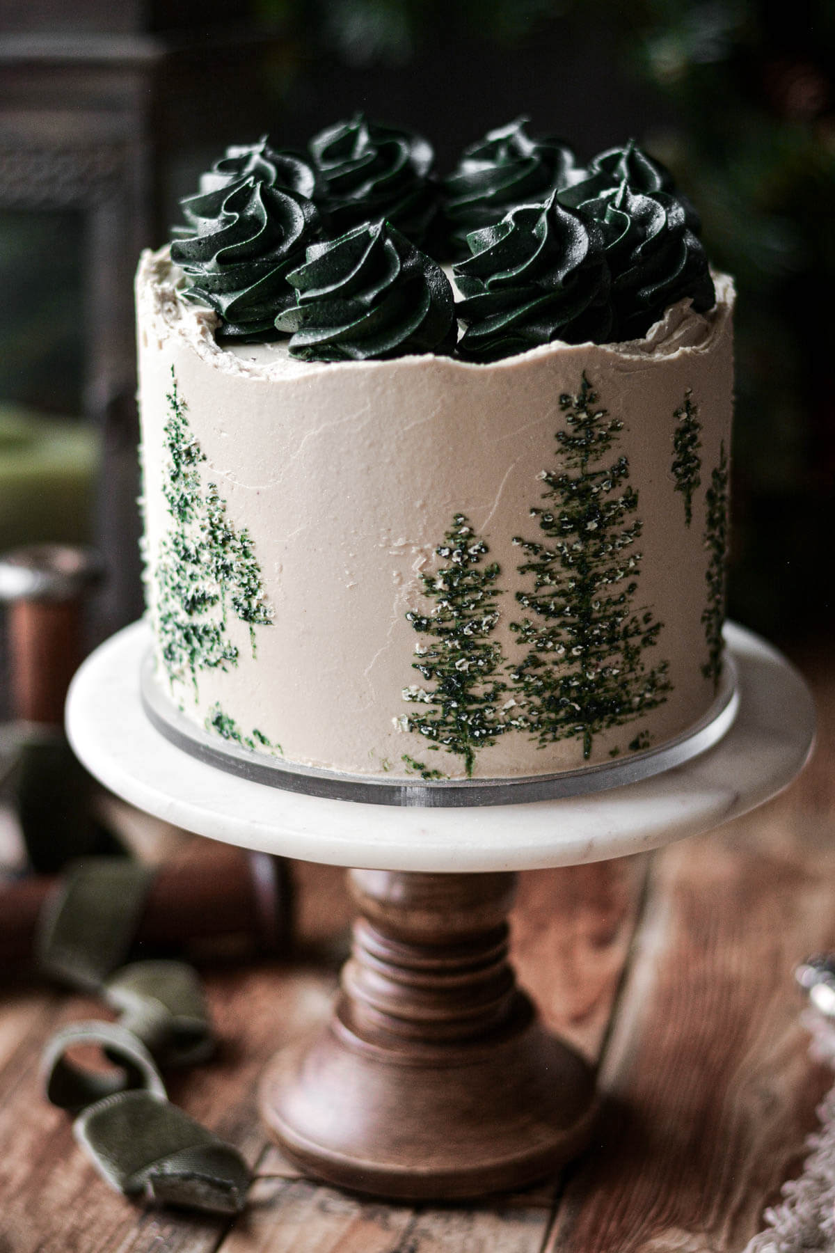 Chocolate maple cake with green evergreen trees painted onto the cake.