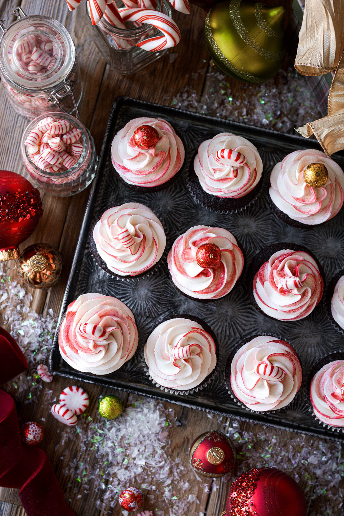 Chocolate peppermint cupcakes surrounded by ornaments and candy canes.