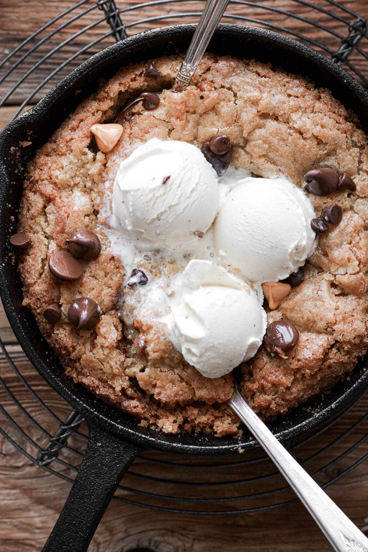 Butterscotch blondies in a skillet with ice cream and two spoons.
