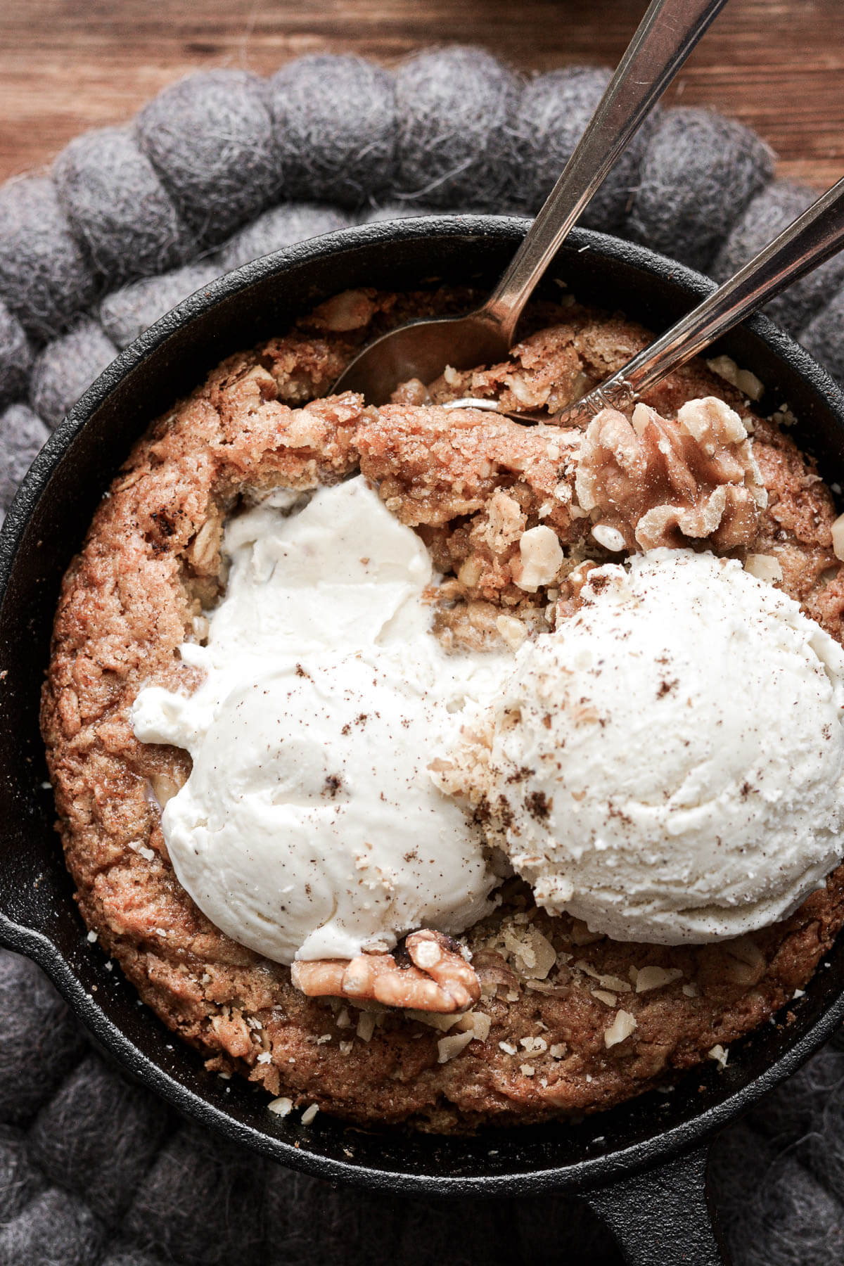 Mini oatmeal walnut skillet cookie topped with ice cream, and two spoons.