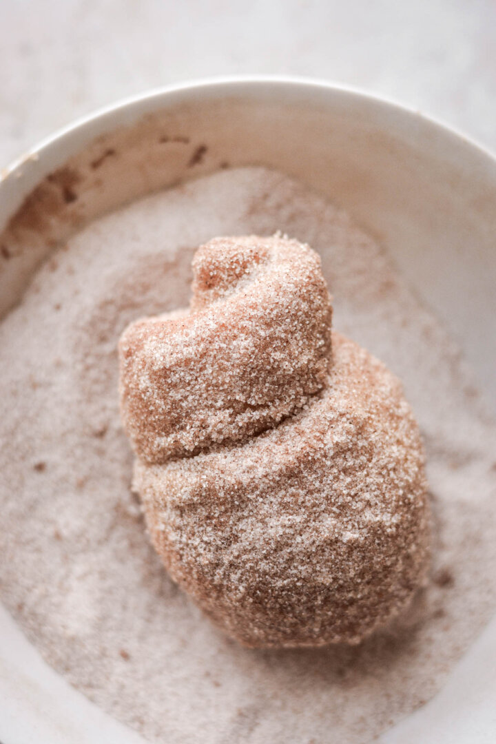 Morning bun in a bowl of cinnamon sugar.