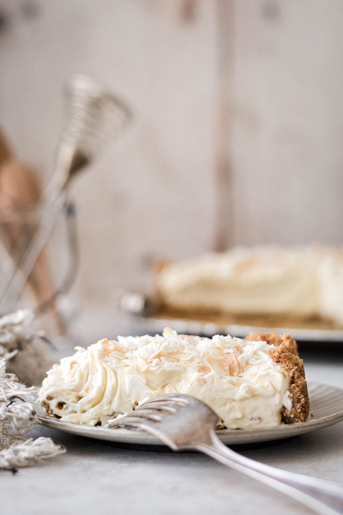 Slice of Bavarian cream pie with toasted coconut on a plate with a silver fork.