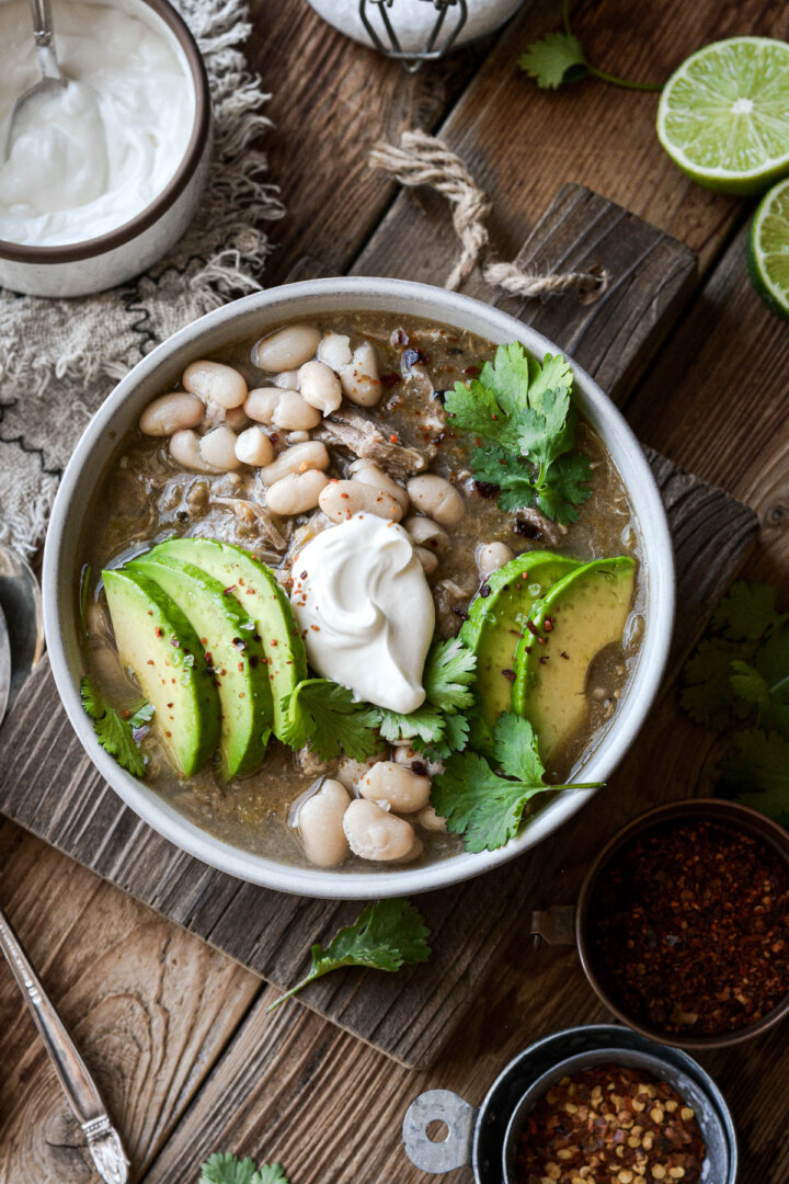 Bowl of pork green chili with avocado slices, beans and sour cream.