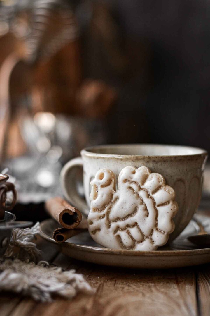 A turkey shaped sugar cookie leaning against an espresso cup.